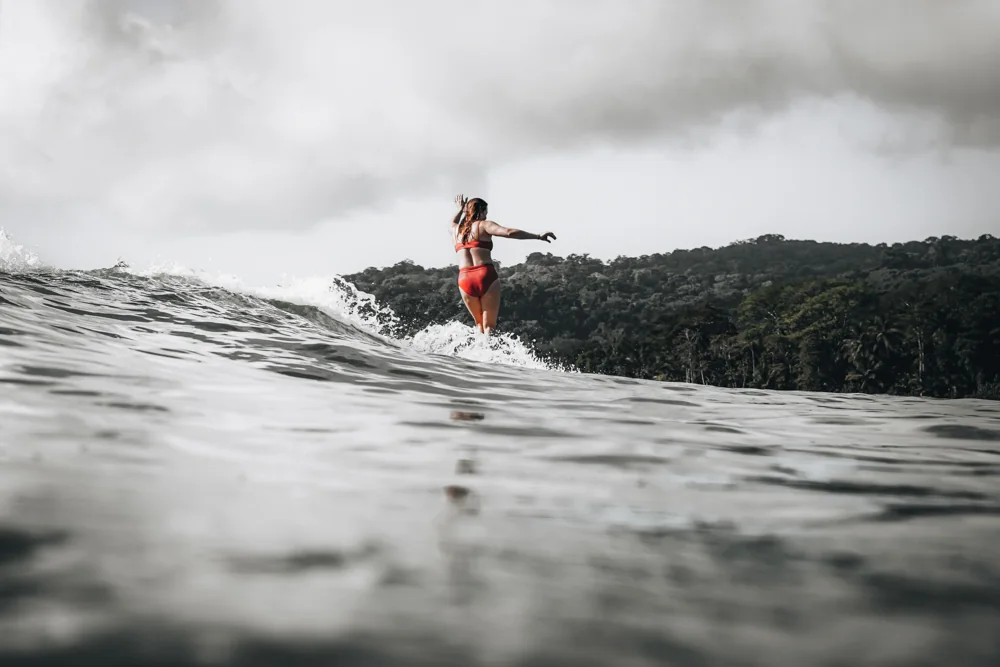 A longboarder in red walking the nose of her board with jungle headlands behind