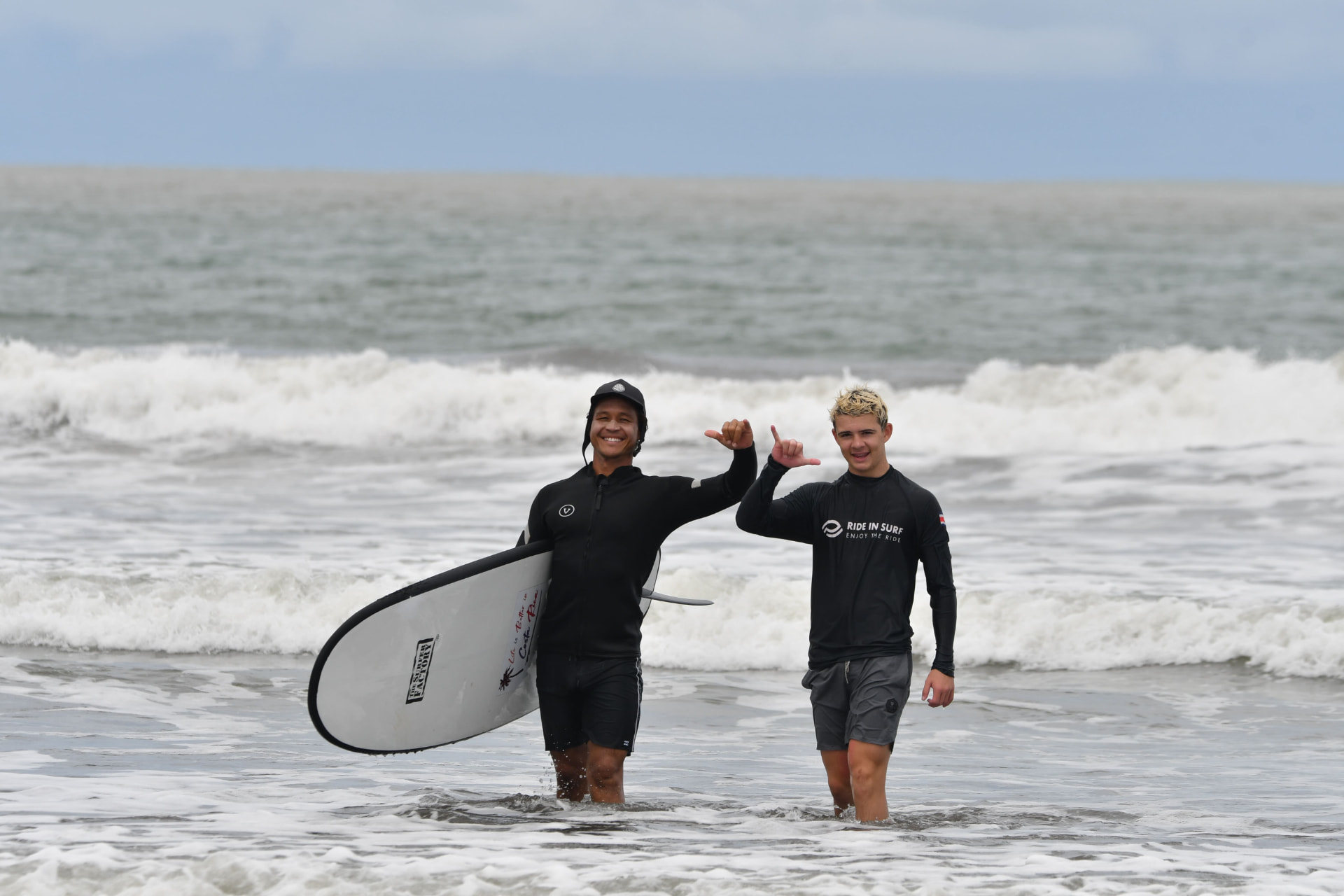 A guest and surf instructor walking out of the surf with a board