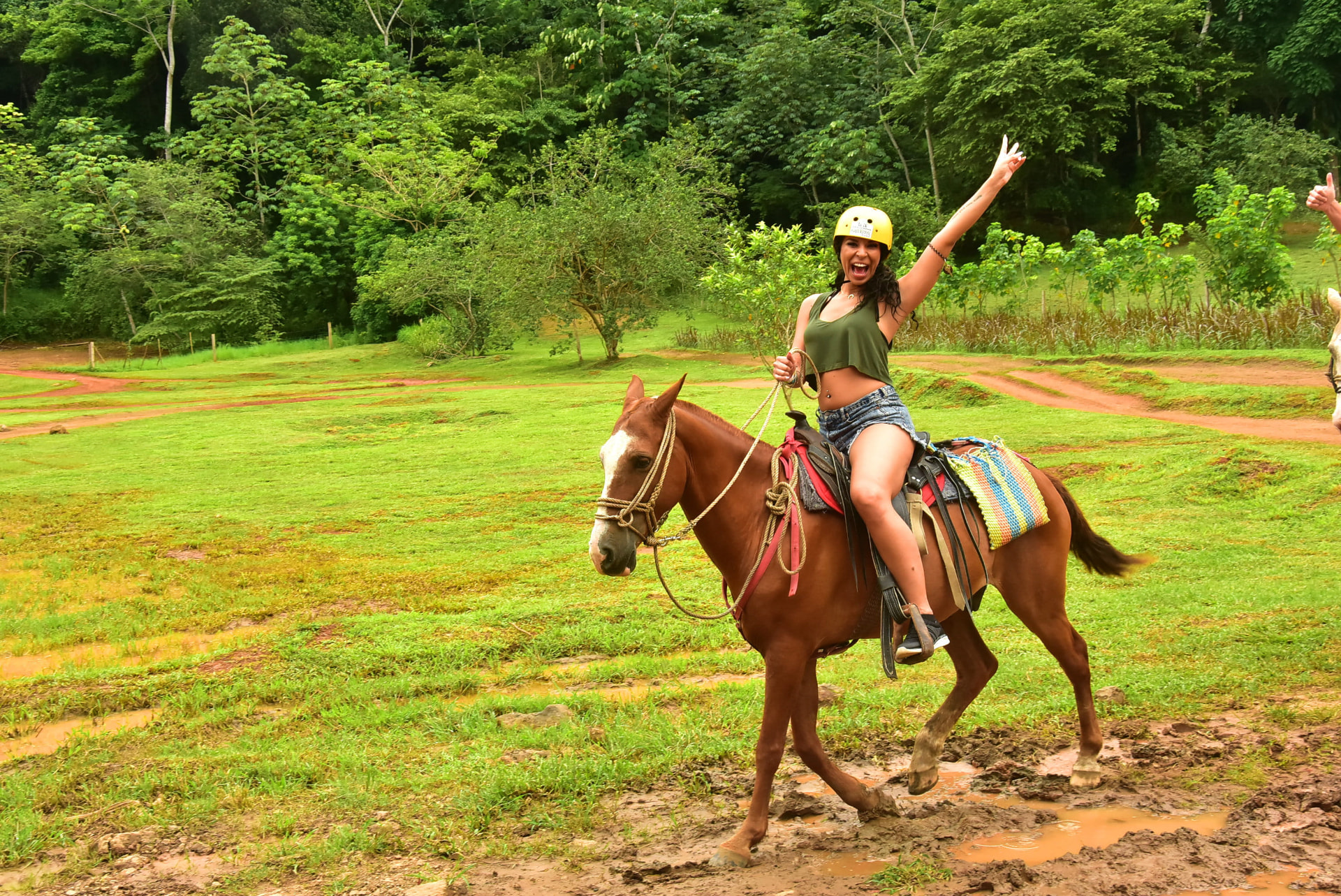 A guest riding a horse across a green pasture with one arm raised