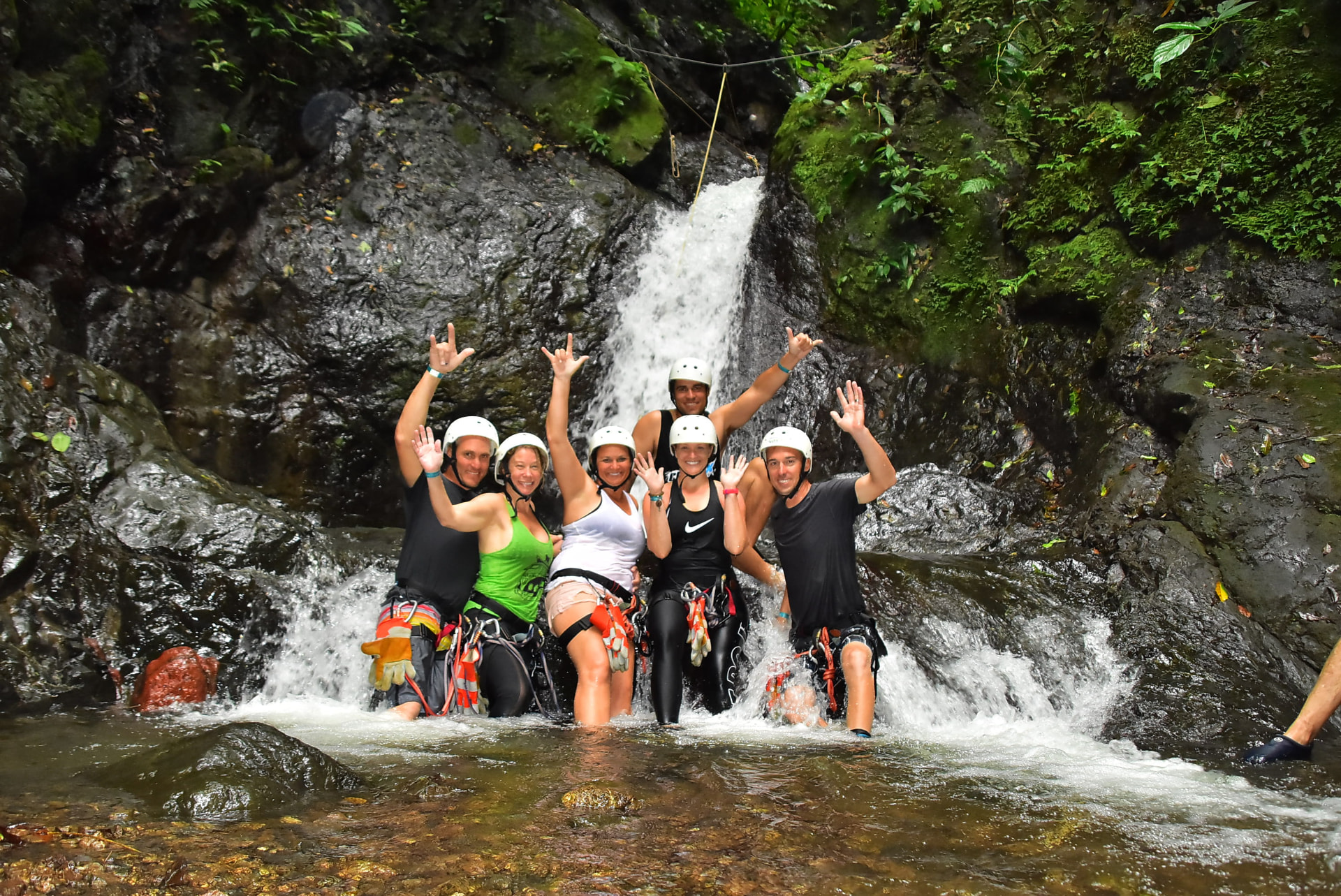 Six guests in helmets and harnesses celebrating beneath a jungle waterfall
