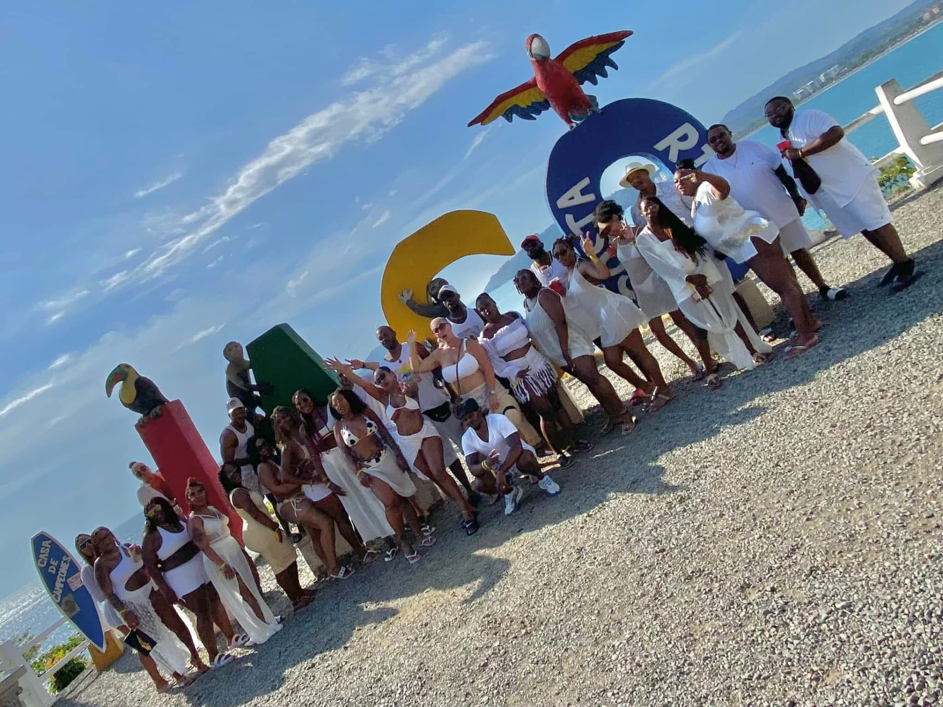 A large group dressed in white posing at the Costa Rica letters by the sea