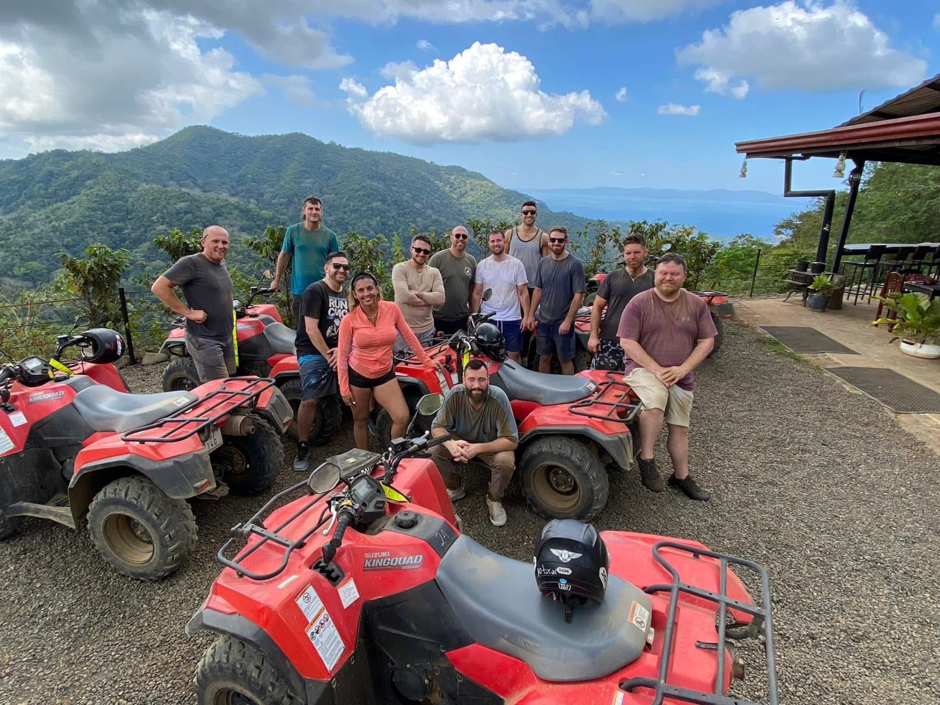 A group of travellers with red quad bikes at a mountain viewpoint over the ocean