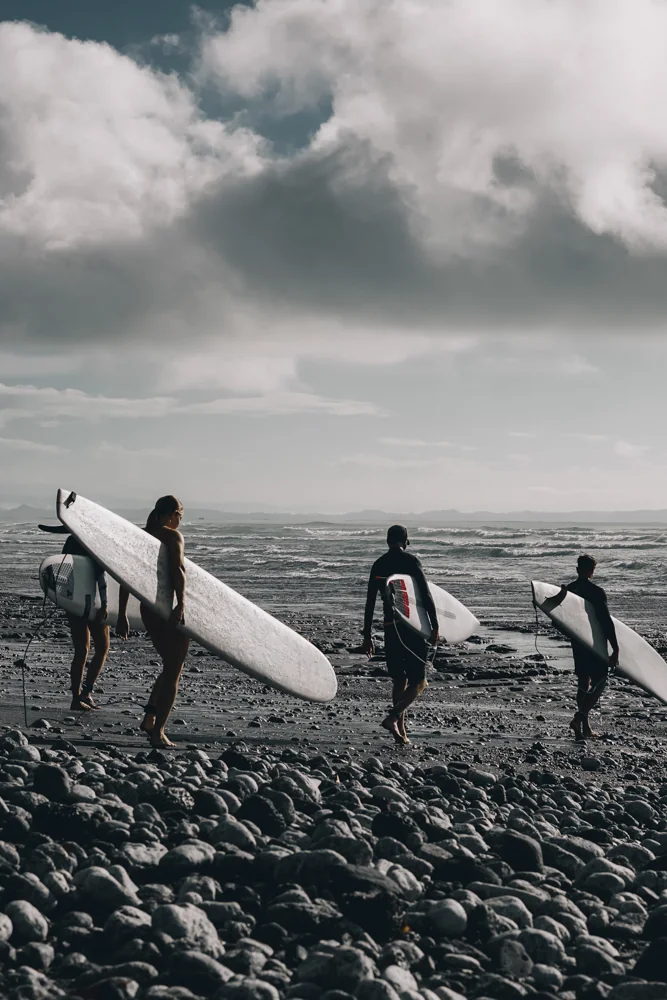Three surfers carrying their boards across a rocky beach towards the waves